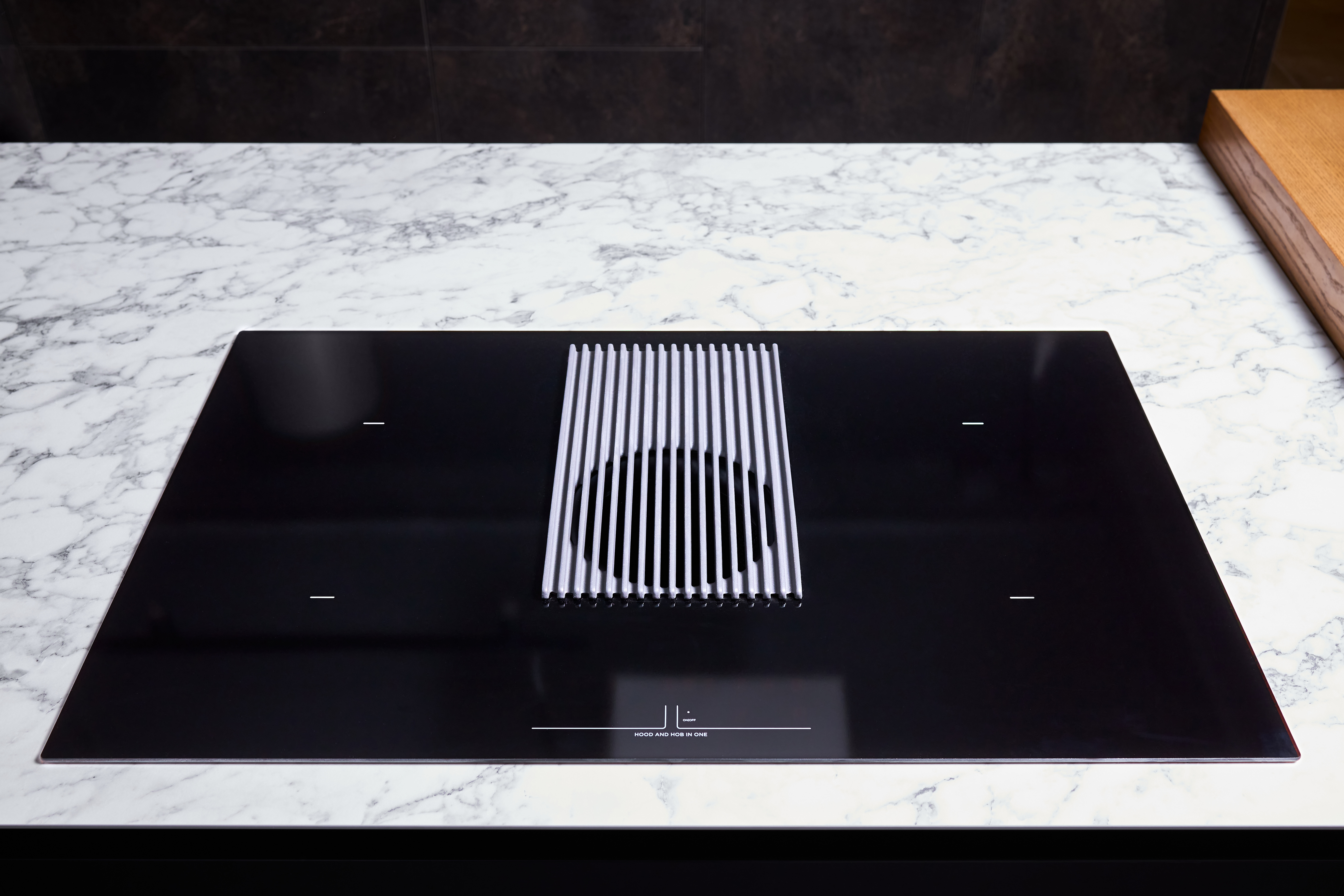 Schwarzer Glaskochfeld-Induktionsherd mit integrierter Haube auf heller Marmor-Arbeitsplatte in moderner Küche.