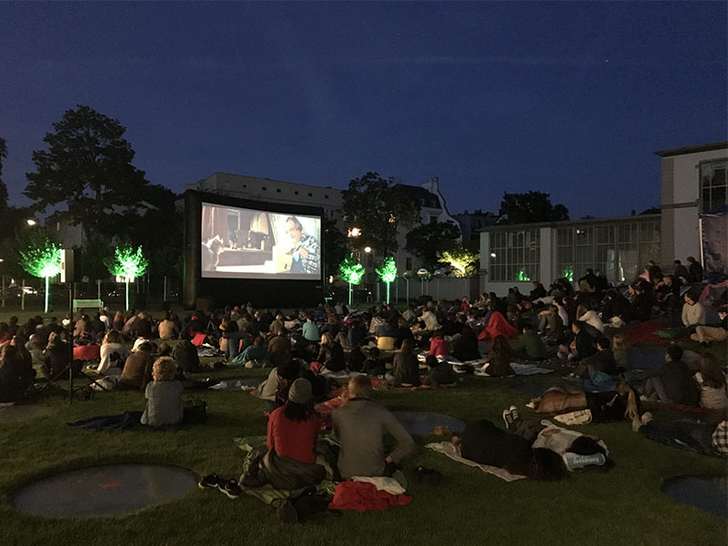 open-air-veranstaltung-planen-und-durchfuehren-in-frankfurt-foto-besucher-sitzen-im-park-auf-boden-und-schauen-film-auf-grosser-leinwand